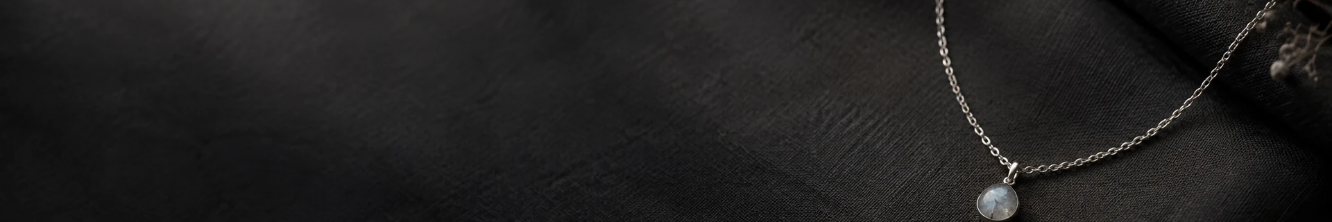 Editorial still life of a fine chain and mineral forms on dark linen for the necklace collection
