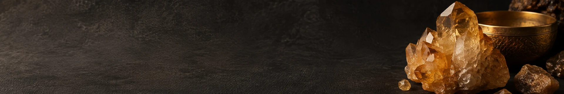 Editorial still life of a honey-coloured mineral, dark stone, and a subtle warm metal detail