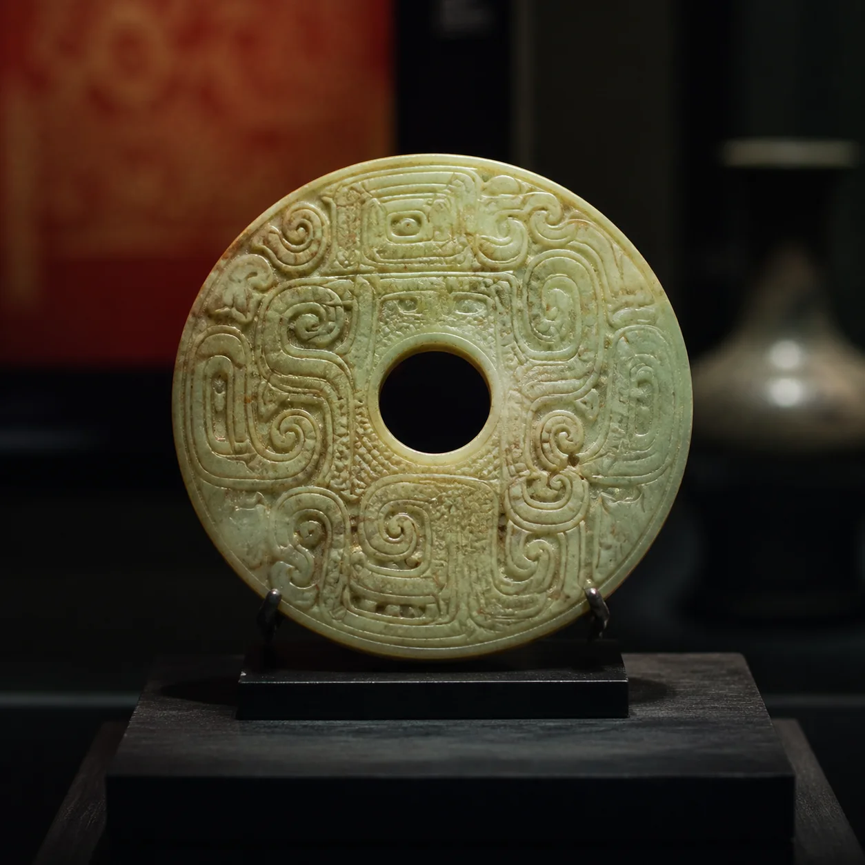 A carved circular jade object displayed on a dark museum plinth
