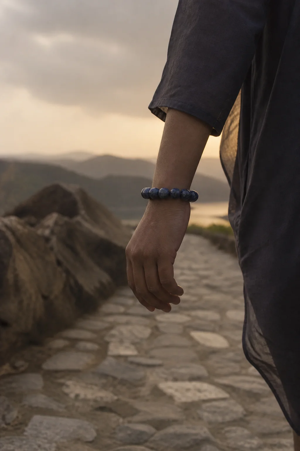 A person carrying a dark blue bracelet while walking along a quiet path in early evening light