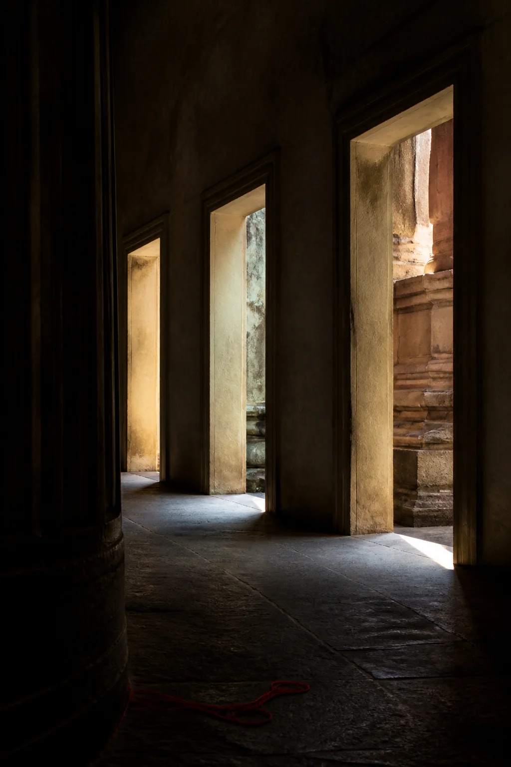 Three quiet doorways in a shadowed corridor, each opening toward a different wash of natural light