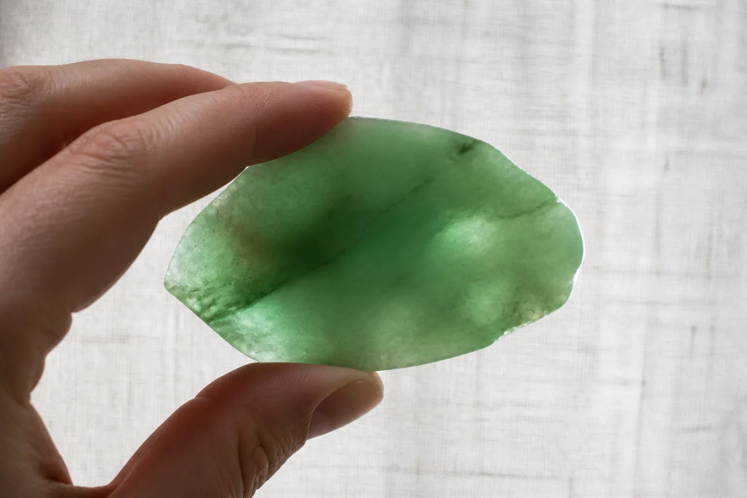 A translucent green jade stone held up to diffuse daylight by a hand
