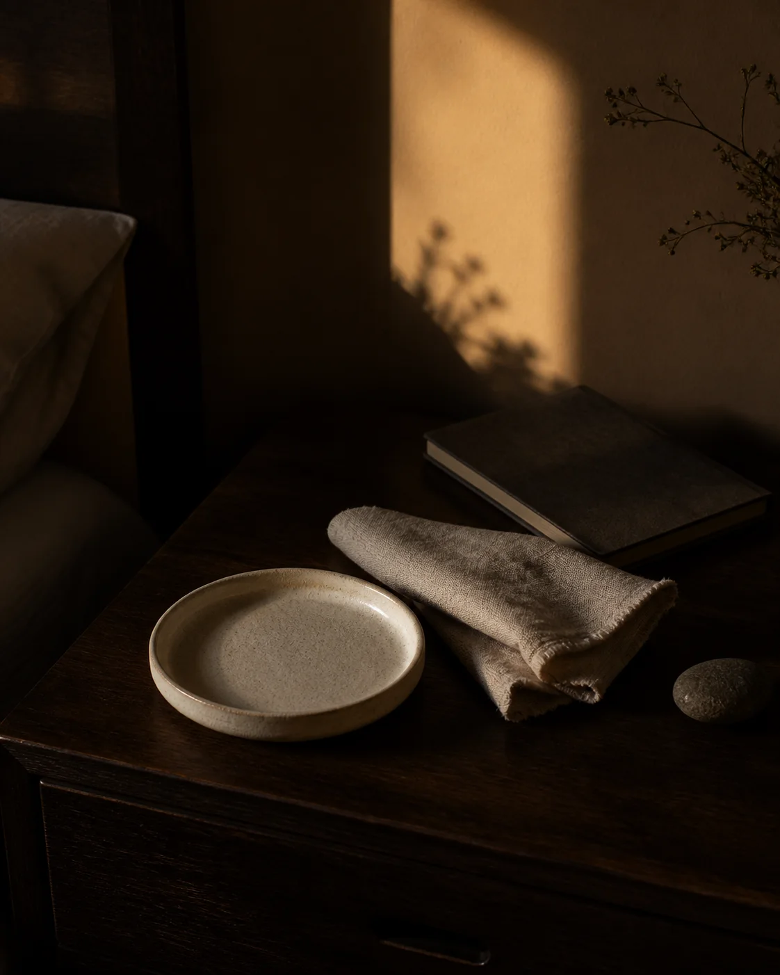 An empty ceramic tray, folded linen, and closed notebook resting on a dark wood table at dusk