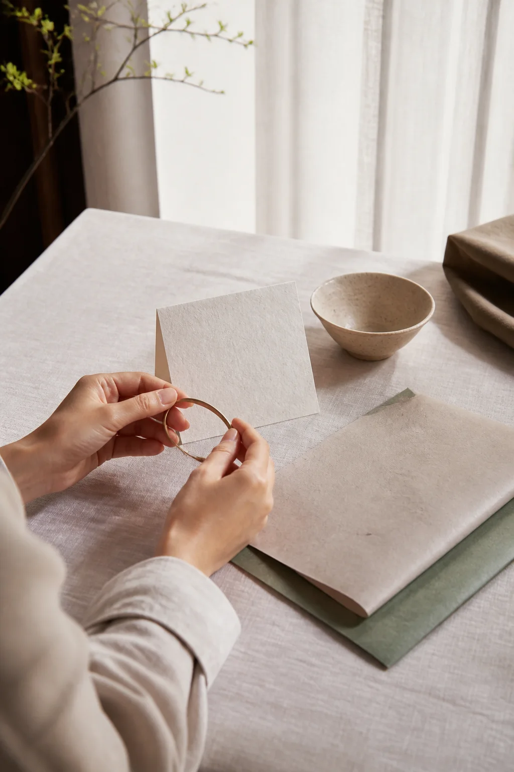 Hands considering a simple gift object beside blank paper and restrained wrapping materials