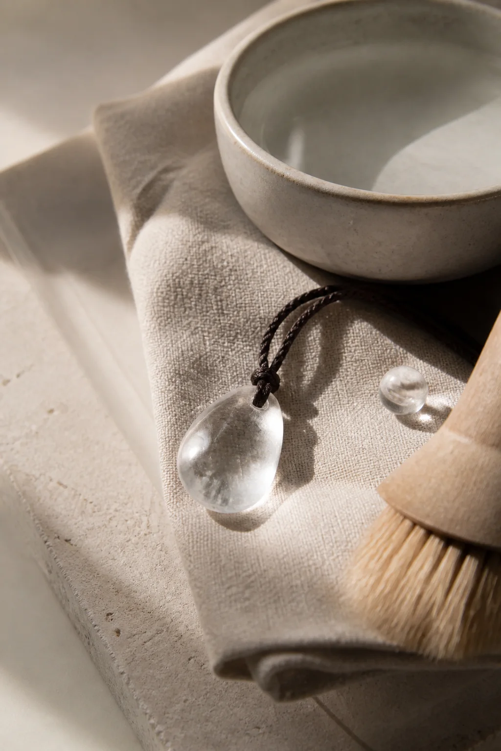 A clear quartz stone resting on linen beside a soft brush and ceramic dish