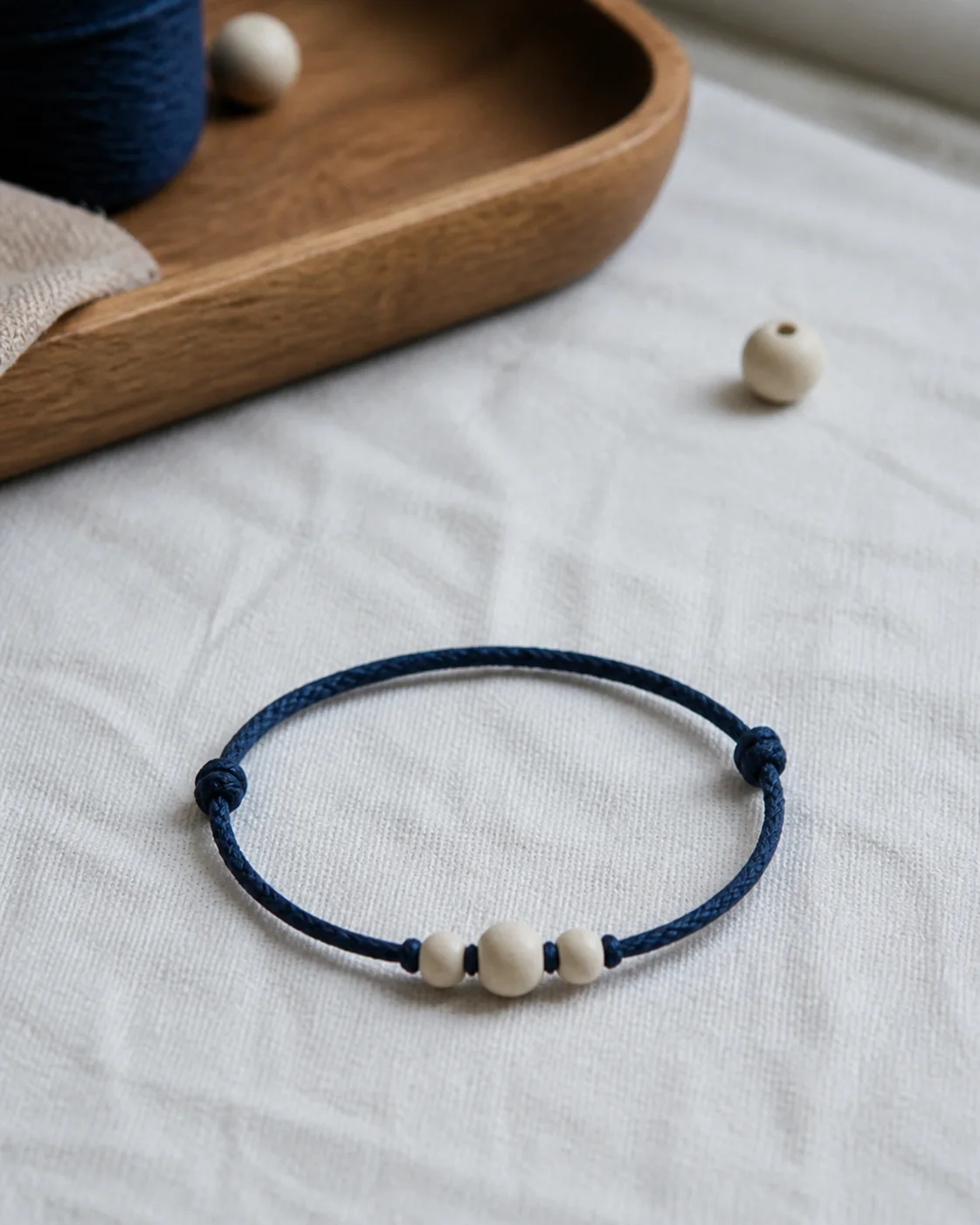 Illustrative still life of a simple indigo cord bracelet with small wooden beads on pale handmade paper