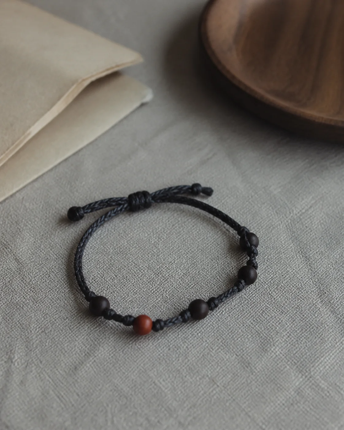 Illustrative still life of a simple charcoal cord bracelet with dark beads on textured grey paper