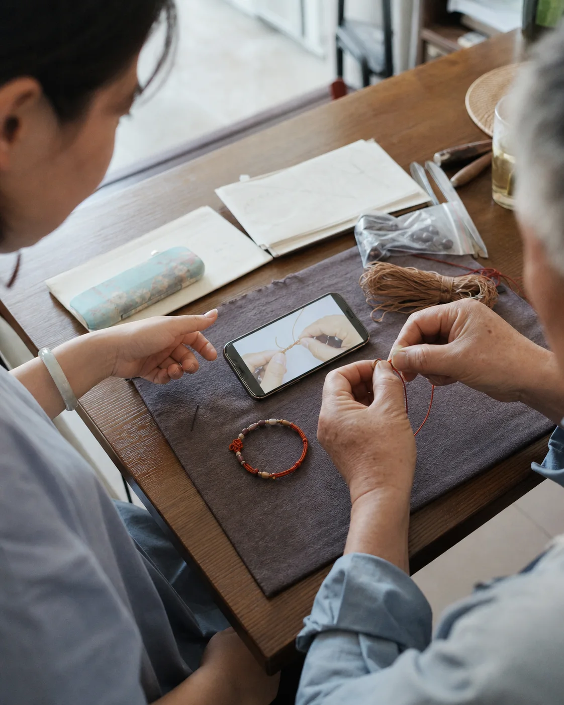 Illustrative scene of a family member showing an older maker a simple bracelet tutorial at a home worktable